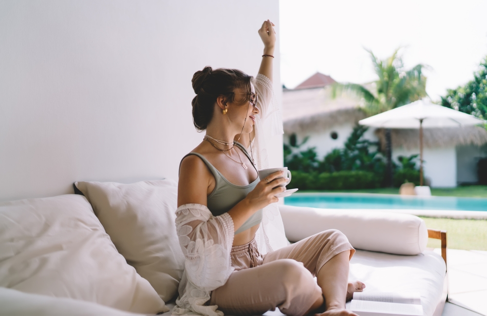 Woman in soft morning light holding a cup of coffee on an outdoor daybed